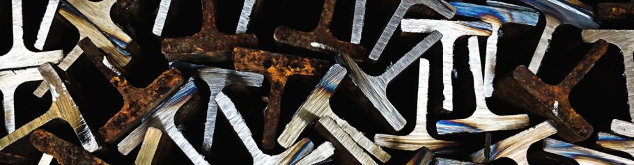 Close-up of interlocking rusted and brushed metal bars forming an abstract, word-like pattern on a dark background.